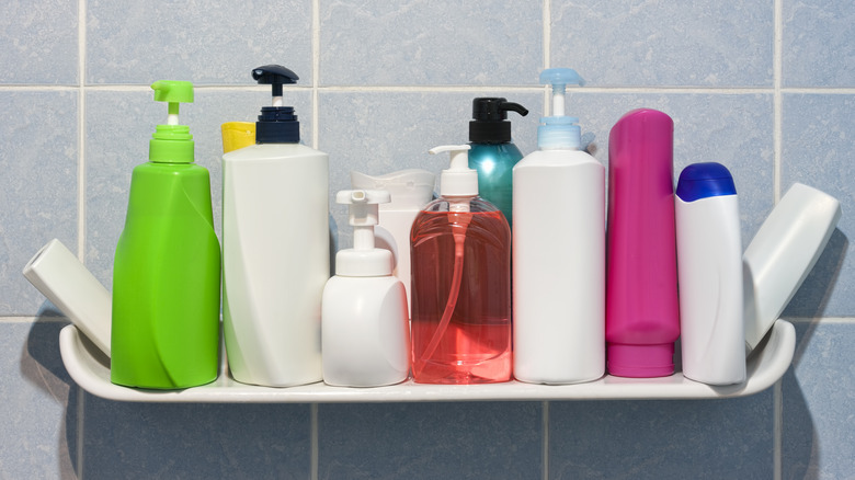 Various bottles and containers of shampoos and conditioners on a shelf against a tiled wall in a bathroom.