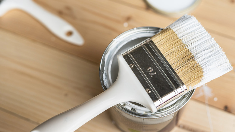 A white brush placed on top of a can of paint