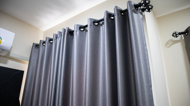 Silver curtain grommets hanging from a black curtain rod