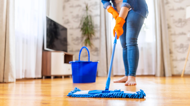 A woman in denim cleaning wood floors with a microfiber mop