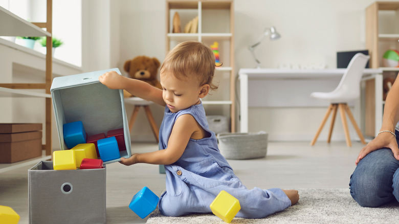 toddler putting away blocks in playroom