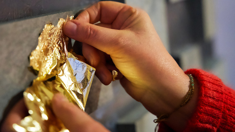 Hands applying gold leaf to a wall