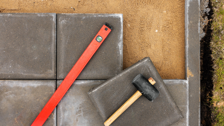 A level and mallet lay on top of an in-progress paver project