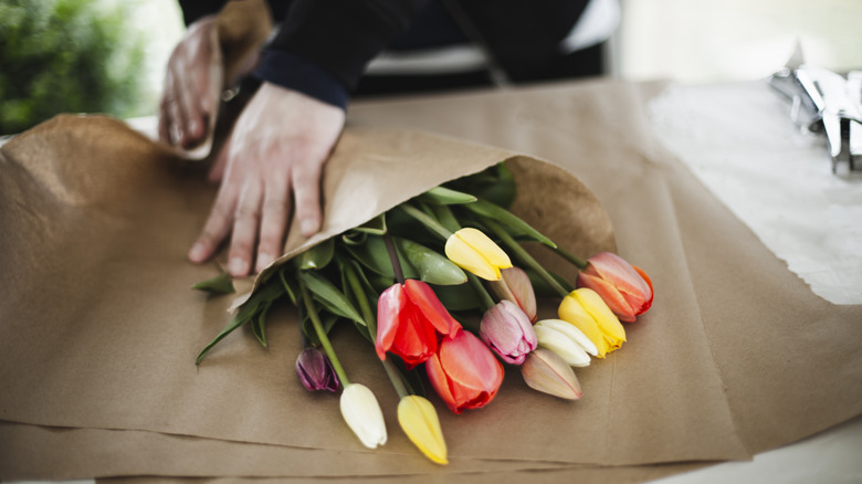 Person wrapping bunch of tulips in brown paper 