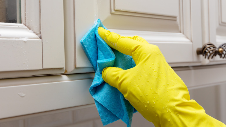 gloved hands scrubbing cabinets