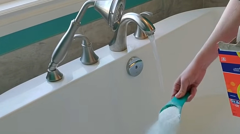 Person pouring laundry detergent beside tub