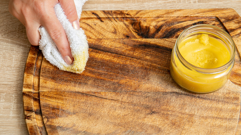 A woman's hand using a white cloth to waterproof a cutting board with beeswax