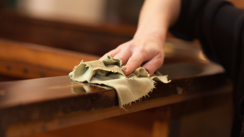 A hand wipes dark wood furniture with a cloth