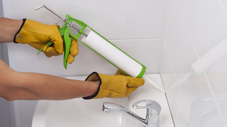 Plumber fills the seam between the sink and tile with a silicone sealant.