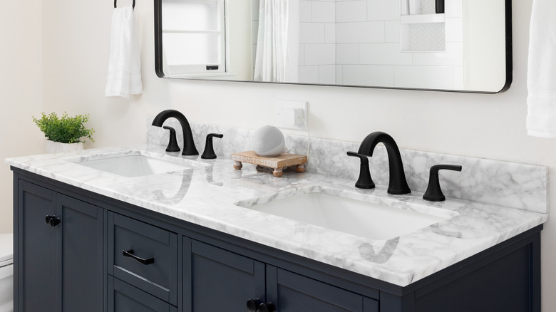 A bathroom with a dark blue vanity cabinet, marble countertop, and large rectangular mirror.