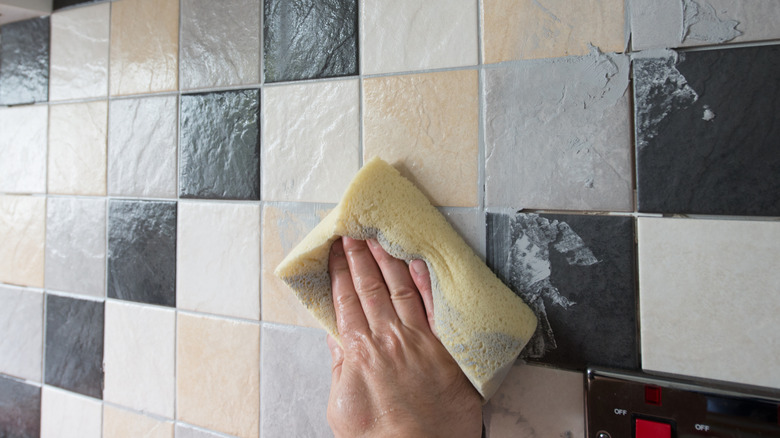 Person using a sponge to wipe grout off tile