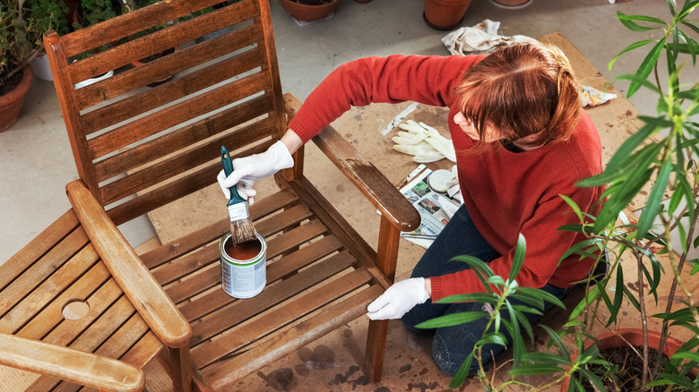 woman staining wooden outdoor chair