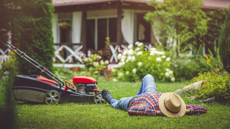 Man lies on grass next to lawnmower