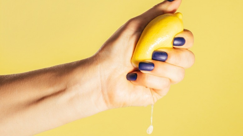 Hand with blue nails squeezing lemon