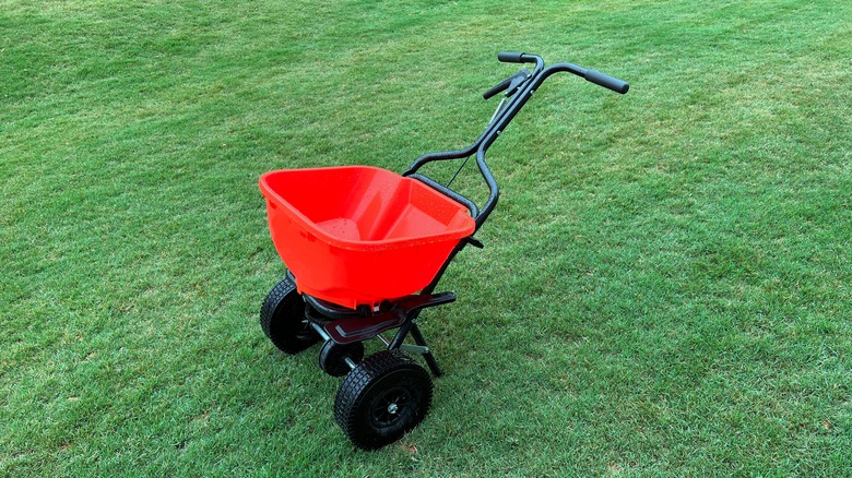 A red fertilizer spreader sitting atop a lush green lawn