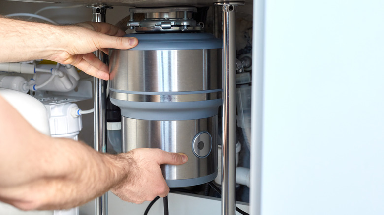 Hands grabbing onto a garbage disposal for repair or installation