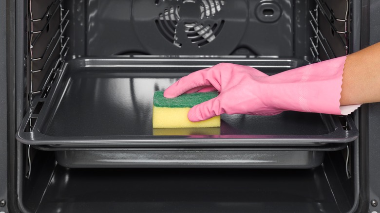 Gloved hand cleaning pan inside oven