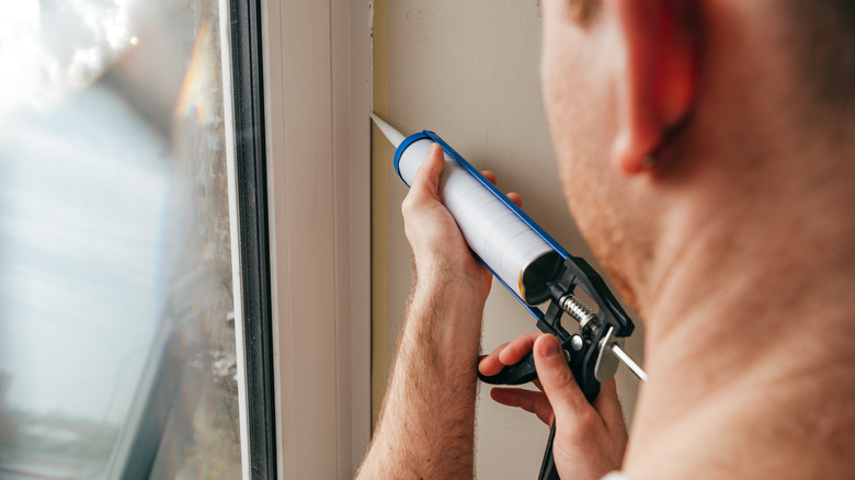 person sealing window with caulk