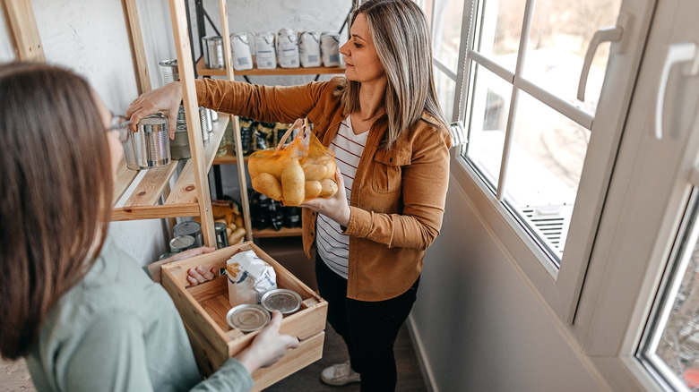 Two woman organizing a simple pantry space with windows on one side