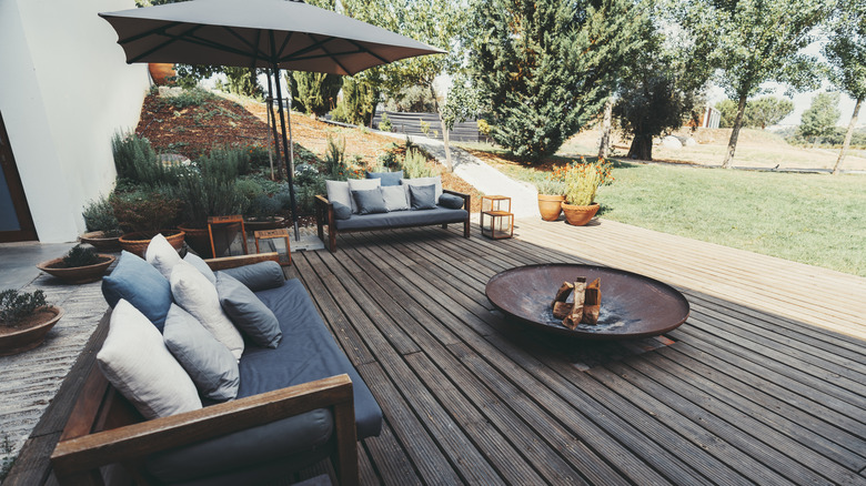 A rustic patio faces a lush backyard on a sunny day