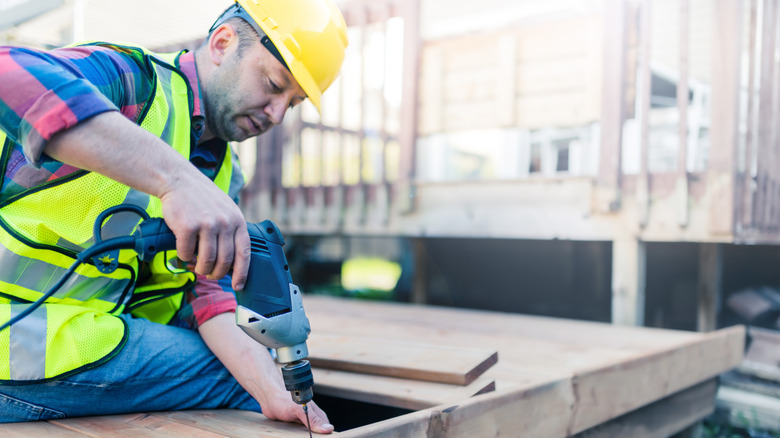 Construction worker screwing down wood deck with electric screw gun