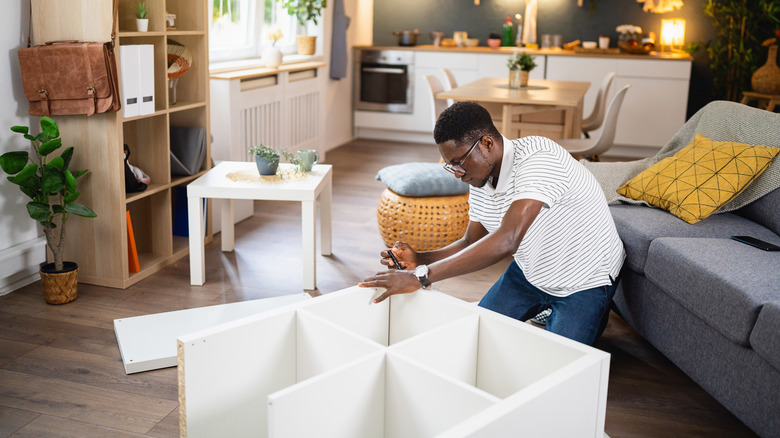 Man assembling white cube storage shelf in living room