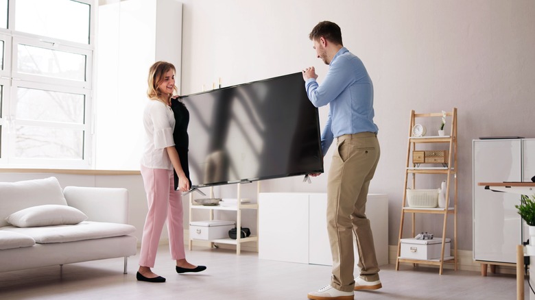 Couple carrying a flat tv screen in a neutral-toned living room