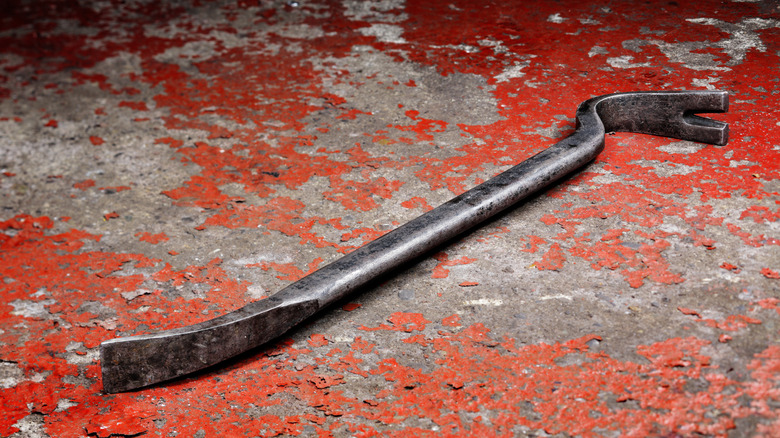 A crowbar placed on concrete with chipped paint