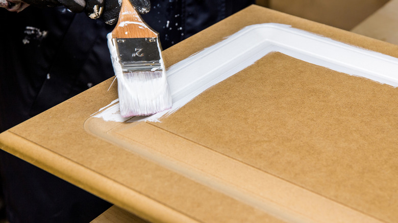 A person paints an MDF cabinet door white