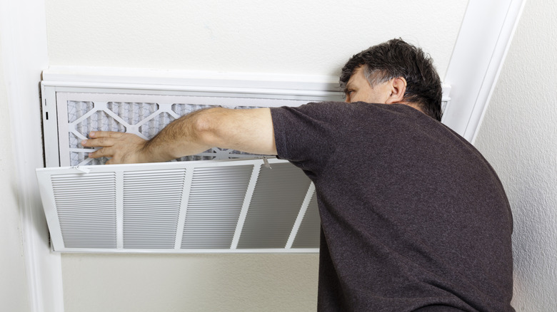 A man in a grey teeshirt replaces an air filter