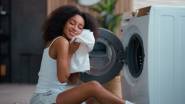 Woman holding soft clean towel to her cheek after washing laundry