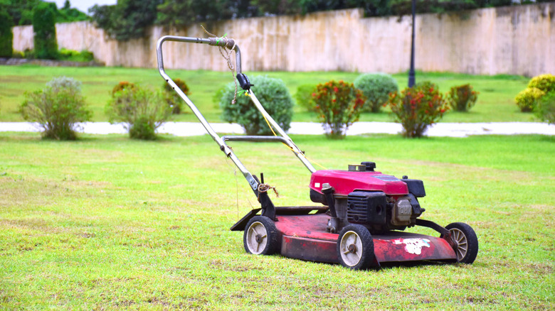 A lawn mower sitting abandoned on a large area of patchy lawn