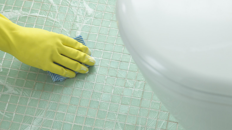 A person cleaning a tiled bathroom floor with a sponge