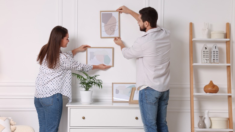 A couple putting picture frames on a wall