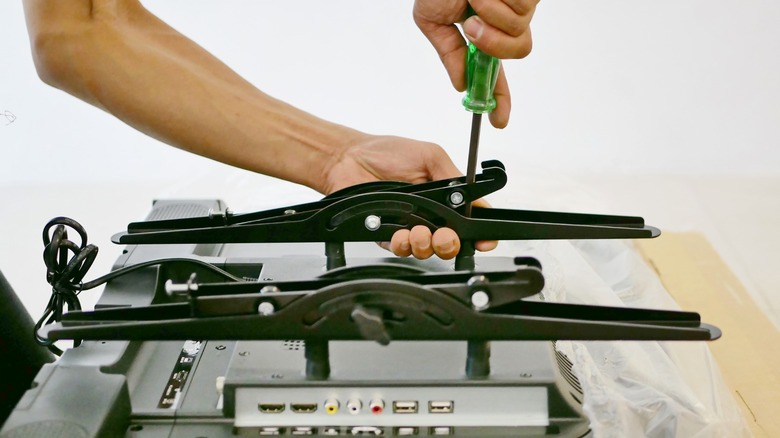 flat screen TV lying face down on table while person hand screws mounting bracket to the back