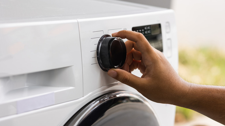 Person's hand turning dial on washer or dryer machine