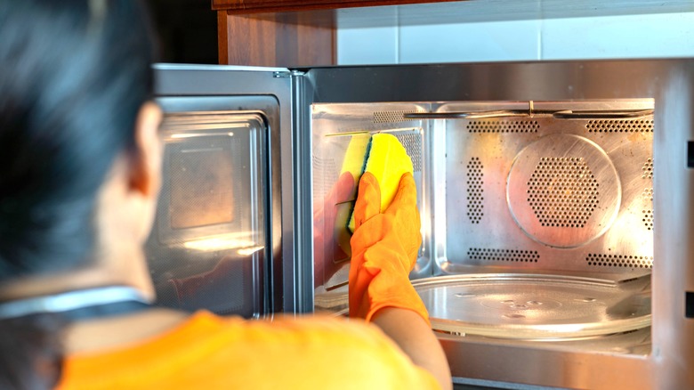 person cleaning microwave with sponge