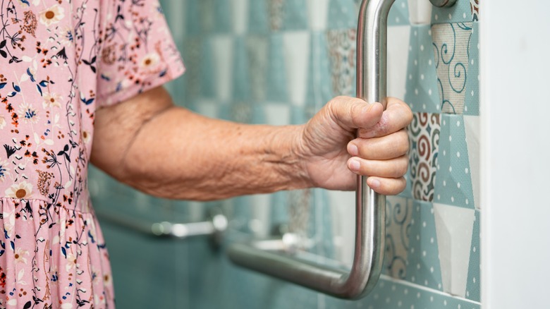 Elderly woman holding bathroom rail