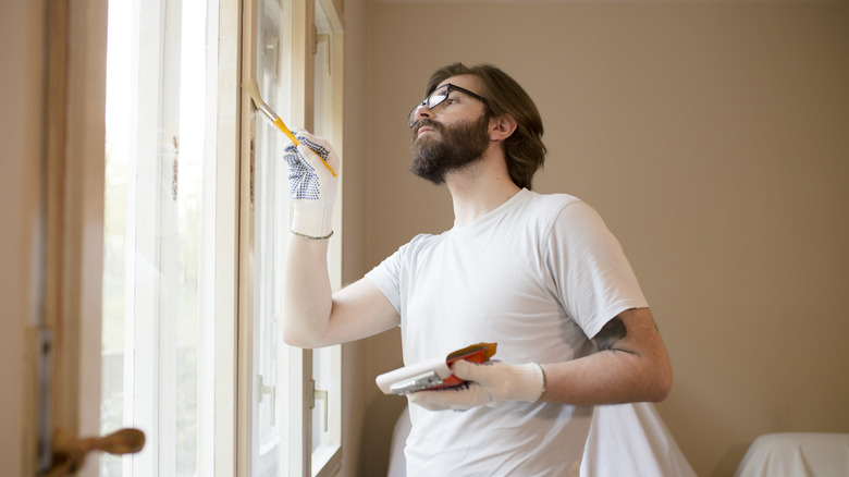 A man with a beard painting the trim around a window