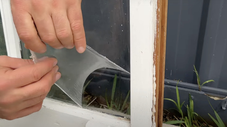 Two hands shown peeling liquid masking off of window glass