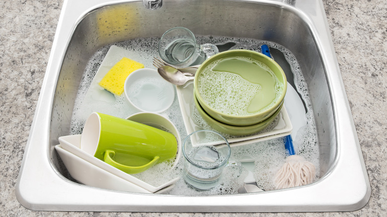 Various types of dishware soaking in soapy water in the kitchen sink