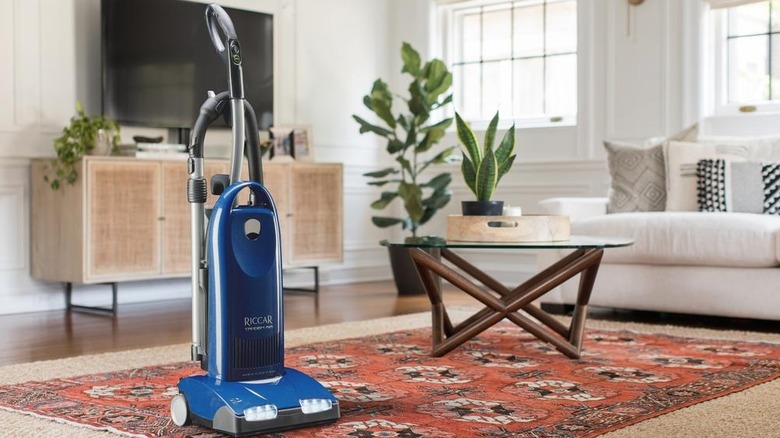 Blue, upright Riccar vacuum cleaner on carpet in furnished room