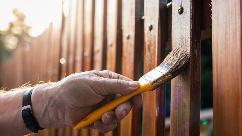 Person holding brush against wood fence