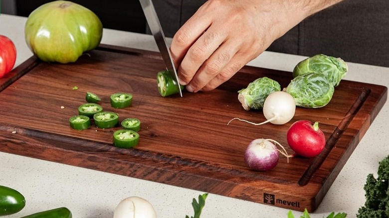 person chopping jalapeño on walnut cutting board