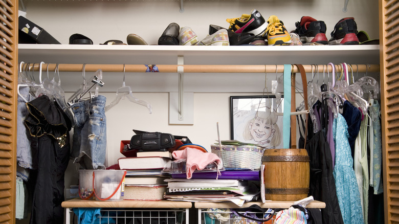 A messy closet with lots of clutter and shoes on top shelf