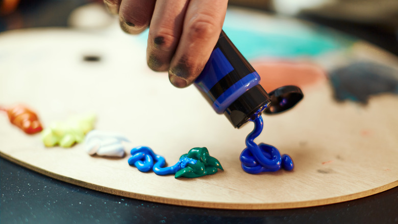 An artist squeezes a tube of blue acrylic paint onto a palette