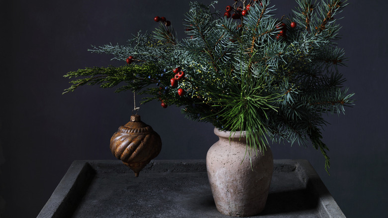 Ornament hanging from pine in a vase with holly berries