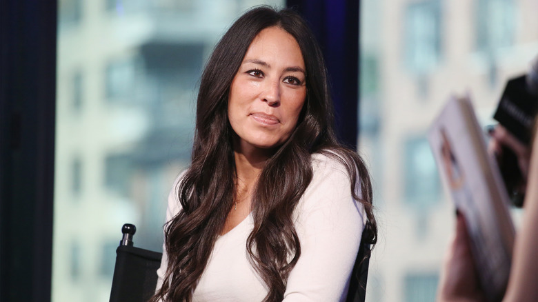 Joanna Gaines wearing a white shirt and sitting in a black chair