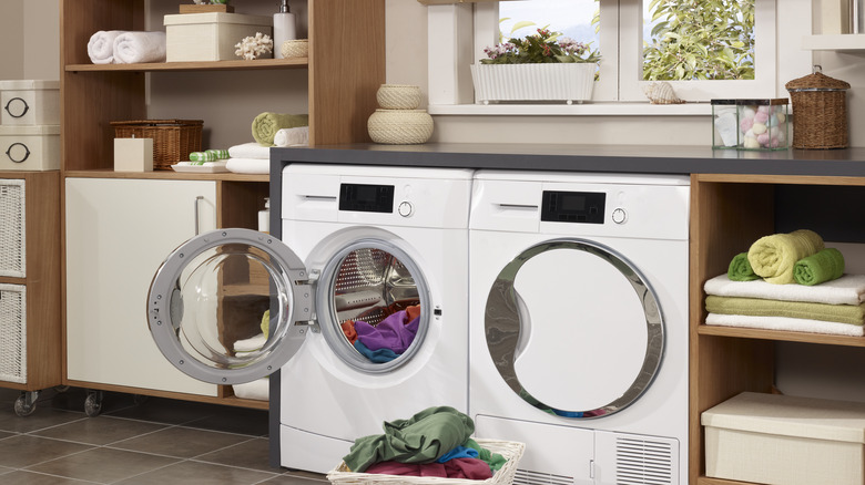 Spacious laundry room with shelves, cabinets, baskets, and jars surrounding washer and dryer in front of a window.