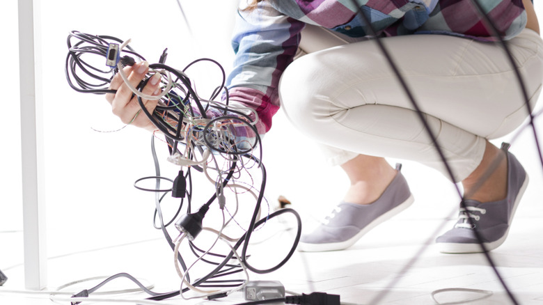 A woman with a handful of disorganized cords under a table.